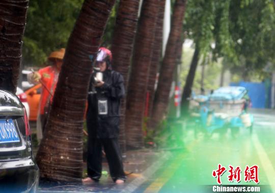 7月16日，一位正在清扫街道残枝落叶的三亚环卫工人在风雨中用餐。　尹海明 摄